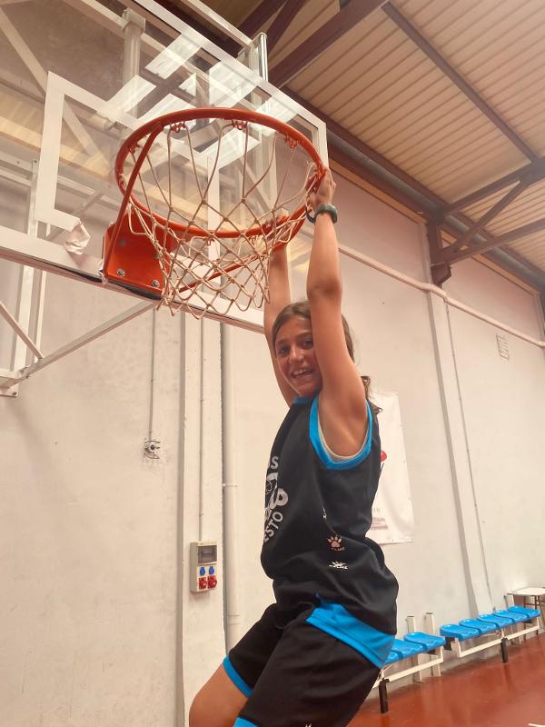 Niña colgada del aro durante un campamento de baloncesto