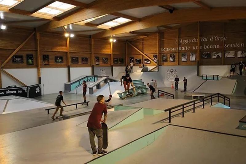 Grupo de jóvenes en un skatepark interior practicando muchos trucos nuevos durante el campamento skate