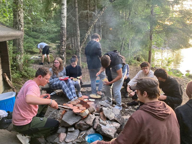 Jóvenes cocinando hamburguesas en el bosque en el campamento de verano en suecia