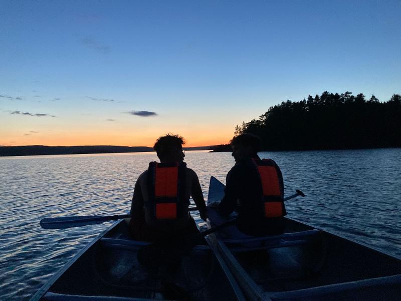 Dos jóvenes en sus canoas con el atardecer de fondo en el campamento de verano en Suecia