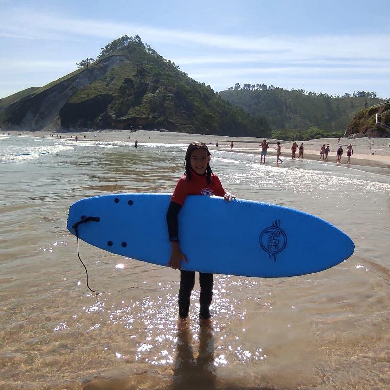 Niña posando con una tabla en la playa durante un campamento de verano asturias