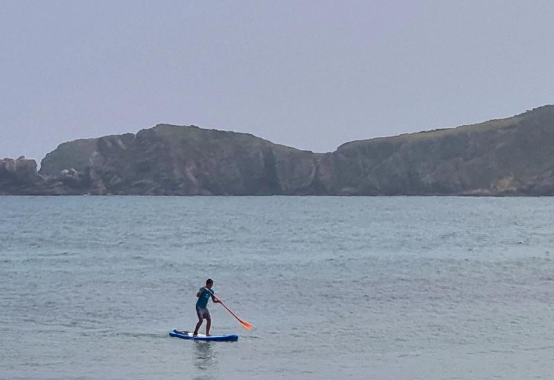 Jóven montado en una tabla de paddle surf en medio del mar en el surf camp bilbao