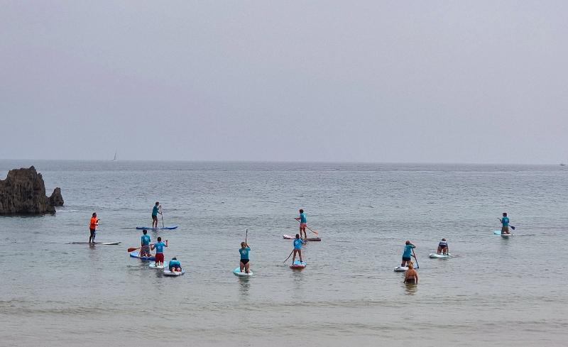 Grupo de niños realizando paddle surf en el mar en calma durante un campamento verano asturias