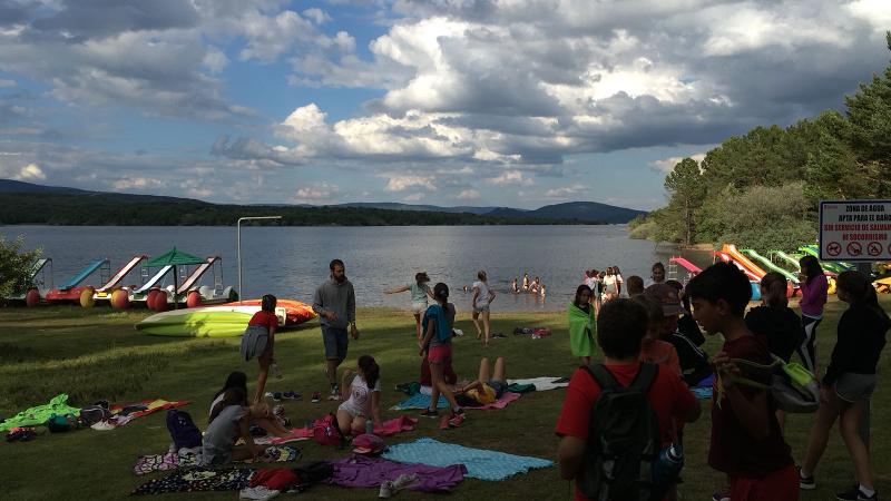 Jóvenes sentados en las toallas mientras otros hablan y otros se bañan en la laguna durante las actividades al aire libre del campamento en Soria