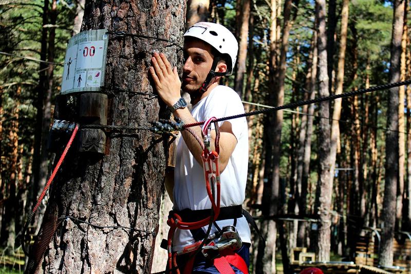 Joven posando divertido detrás de un tronco mientras realiza su prueba en el parque multiaventura del campamento en Soria