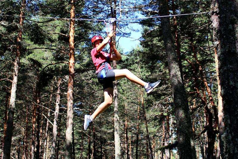 Joven lanzándose en tirolina en el parque multiaventura del campamento en Soria