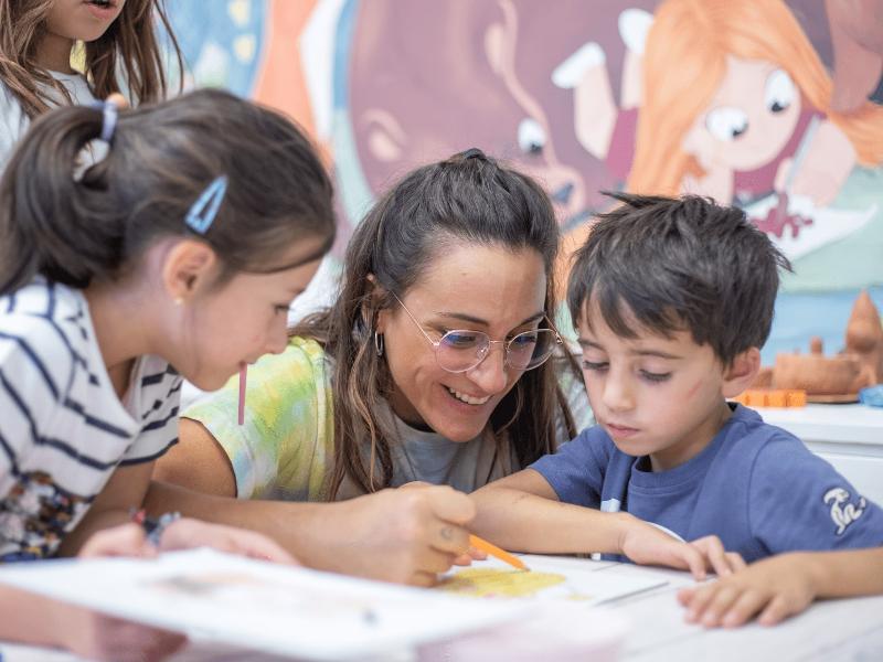 Monitora enseñando a dibujar a dos pequeños participantes durante un campamento de verano burgos