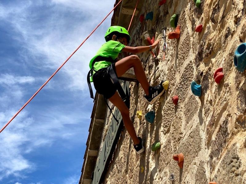 Niño del campamento de verano en la montaña practicando una actividad de escalada en el rocódromo con el material de protección