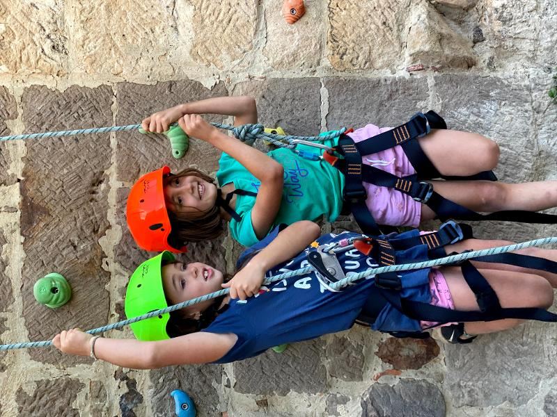 Dos niñas felices después de haber llegado a la cima en la actividad de escalada del campamento de aventura