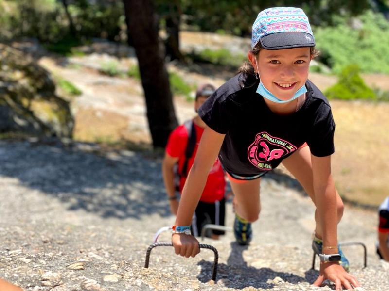 Niña sonriente practicando una actividad de escalada en el entono natural del campamento de atletismo