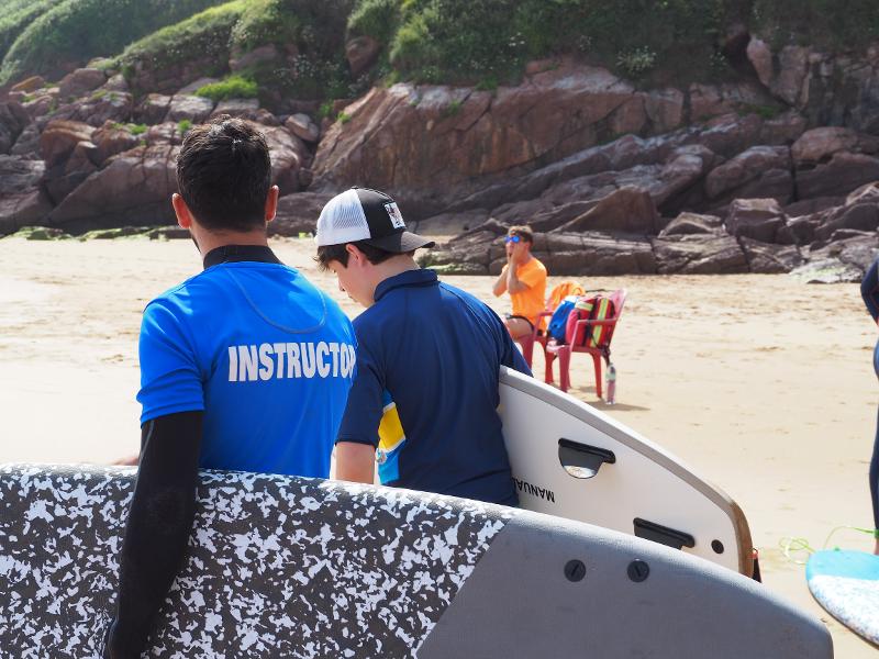 Monitor y participante del campamento de verano Asturias con sus tablas de surf en la playa