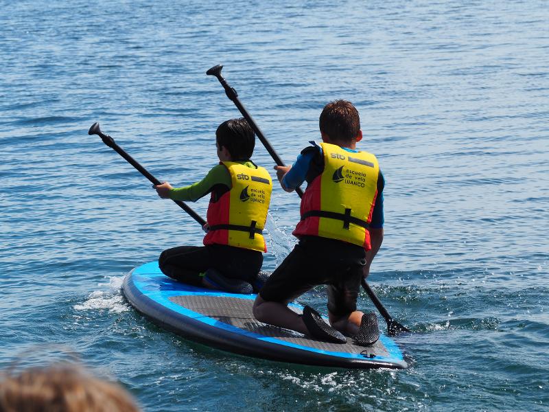 Dos chicos remando encima de una tabla en el campamento asturias