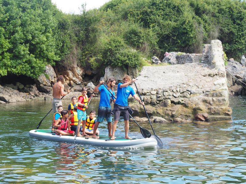 Grupo de niños remando junto con los monitores en la tabla de SUP en una de las escapadas del campamento en Asturias