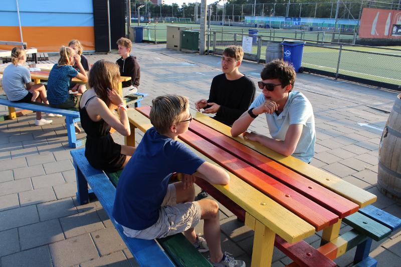 Jóvenes sentado en mesas de picnic conversando durante la pausa para practicar idiomas