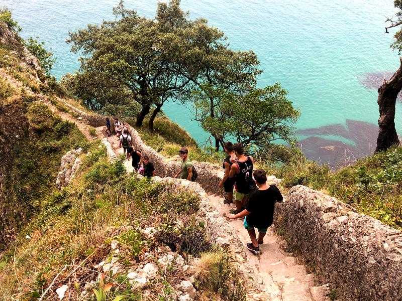 Jóvenes caminando por unas escaleras de piedras para llegar a una cala en una excursión del campamento