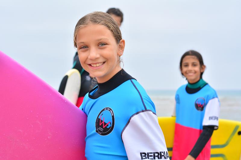 Niñas felices sonriendo con la tabla de surf debajo del brazo después de su sesión diaria en el campamento en Cantabria