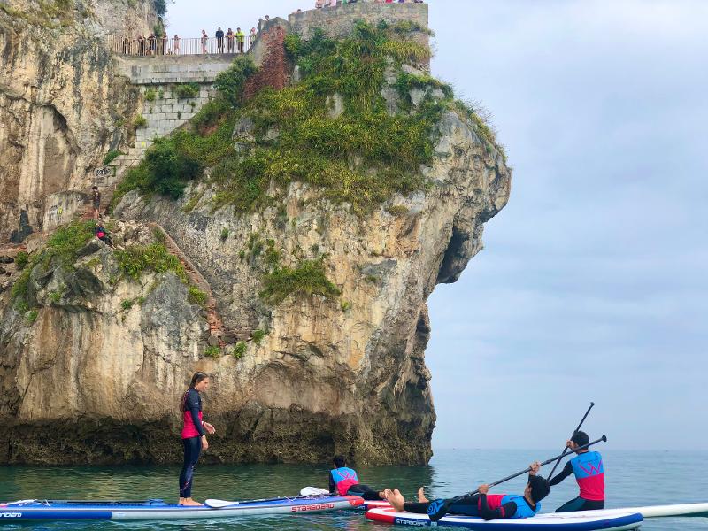 Grupo de jóvenes descansando en las tablas de paddle surf dentro del mar en el campamento en Cantabria