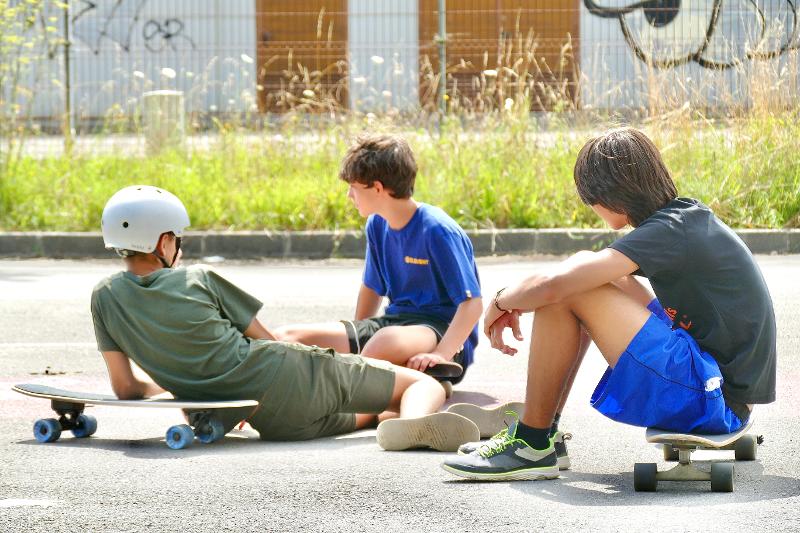 Tres niños sentados con los monopatines descansando de la clase de skate en el campamento de surf en Cantabria