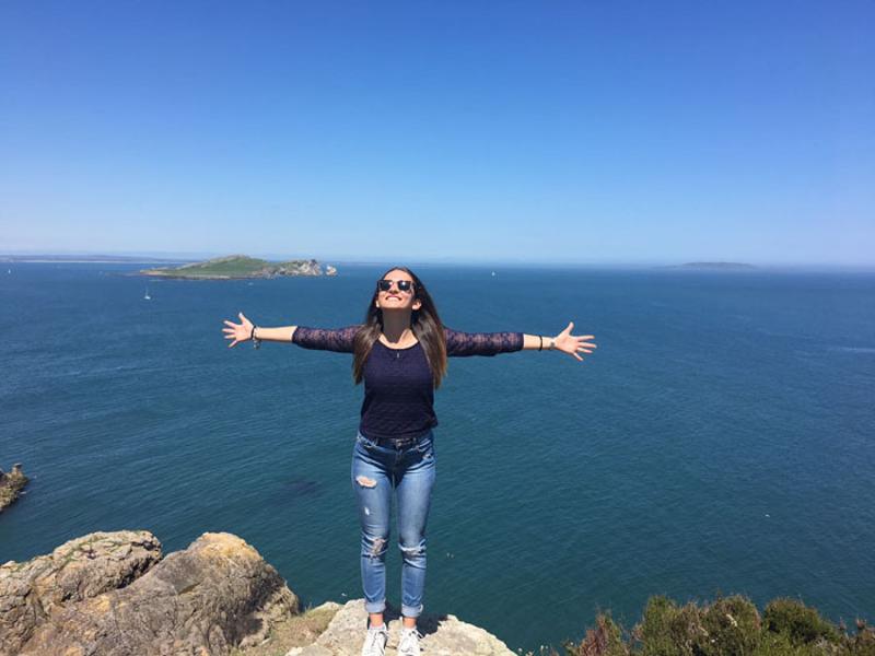 Chica con los brazos abiertos frente al mar posando para una foto en el curso de ingles en dublin 