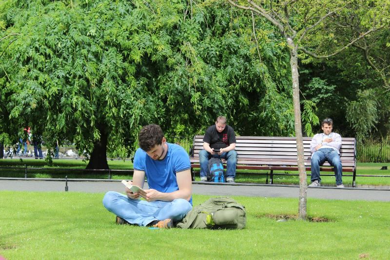 Joven sentado en el césped leyendo en el curso de ingles en irlanda en verano