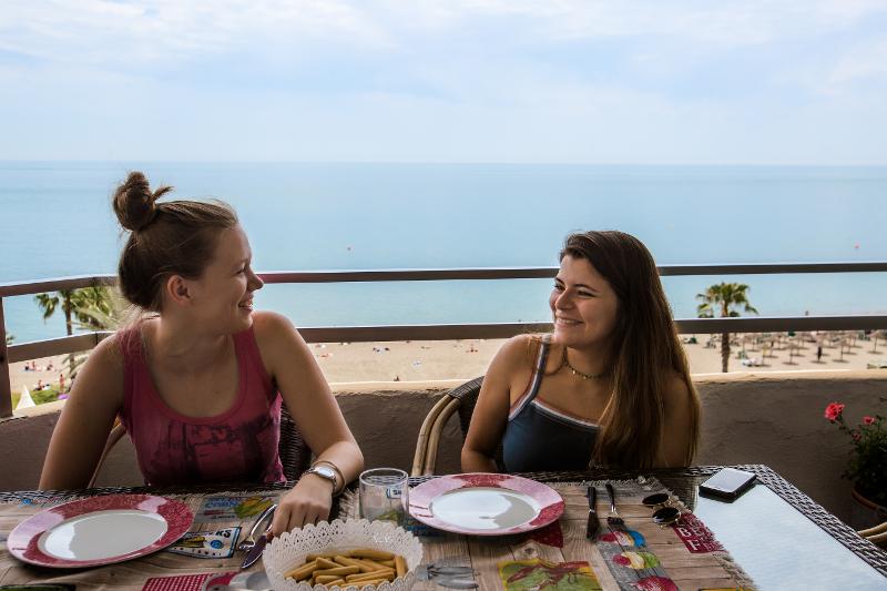 Dos chicas posando en un balcón con la playa de fondo durante los camapmentos de verano de 15-18 años