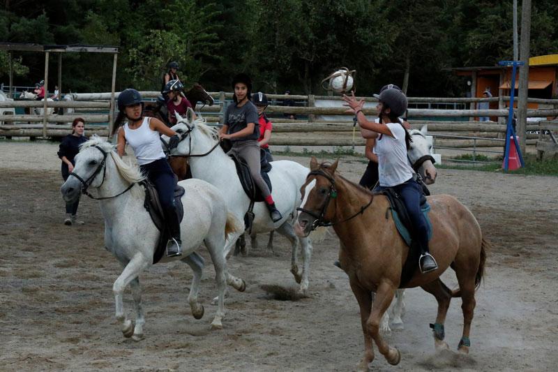 Grupo de participantes del campamento equitación en equipos haciendo un partido de horseball en las pistas exteriores