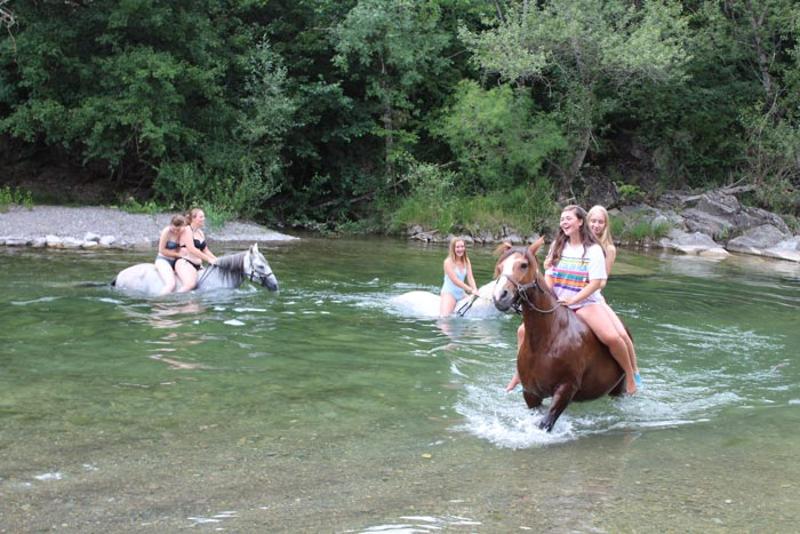 un grupo de jovenes montando a caballo en un lago en un  campamento hipico