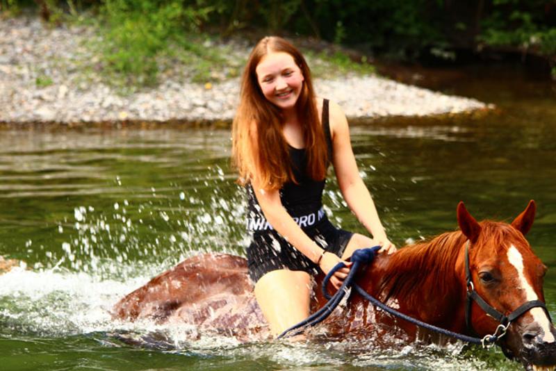 una niña subida a un caballo en un rio en un campamento hipico