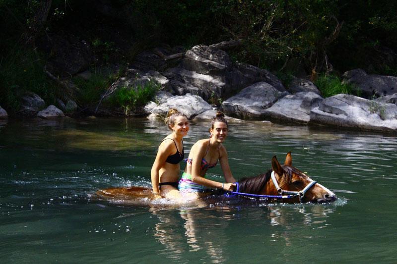 dos jovenes subidas en un caballo nadando en un campamento hipico