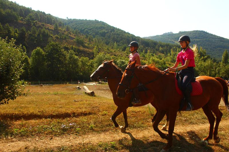 Dos niñas subidas a caballos en una montaña en un campamento hipico