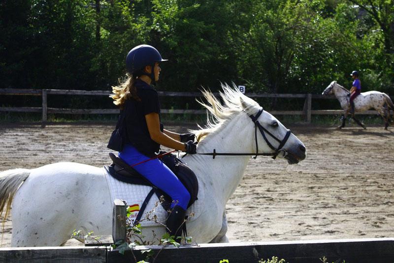 una niña trotando a caballo en un campamento hipico