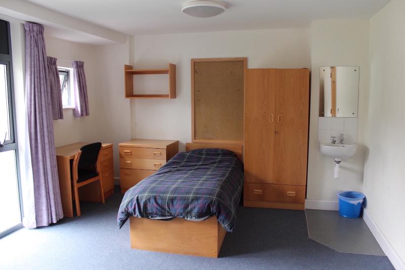 Habitación con cama, armario, cómoda, escritorio y lavabo en el curso de ingles en inglaterra