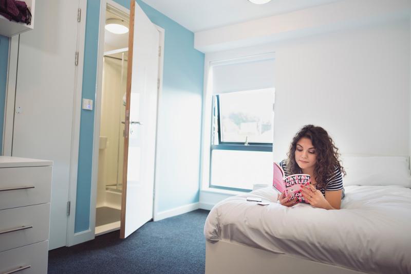 Chica leyendo en su habitación acostada en la cama en el curso ingles en inglaterra
