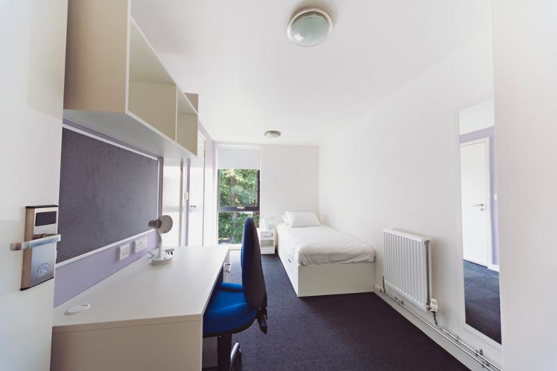 Habitación individual con cama, espejo y escritorio con silla en el curso ingles en inglaterra