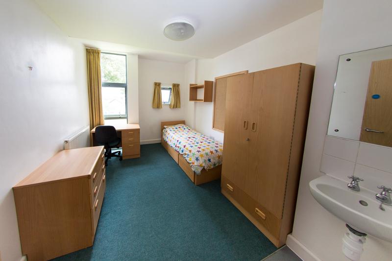Habitación individual con escritorio con silla, armario, cómoda y lavabo en el curso ingles en extranjero