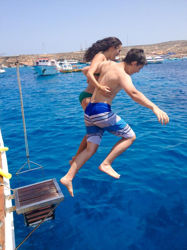 Chico y chica saltando juntos al agua desde un barco en los cursos ingles verano malta