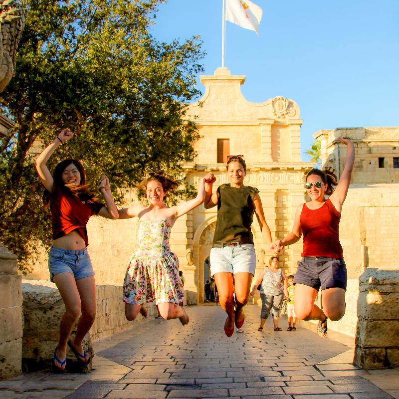 Cuatro chicas cogidas de la mano saltando en los cursos ingles verano malta