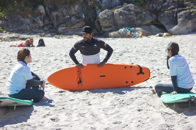 Dos participantes junto al instructor dando una clase personalizada de surf en la arena del surfcamp gran canaria