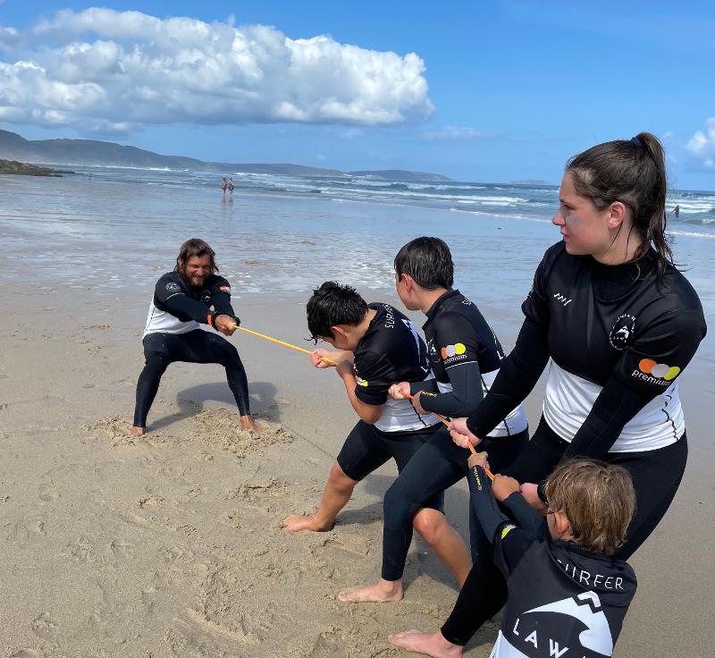 Grupo de participantes jugando a estirar la cuerda en la orilla del surf camp gran canaria