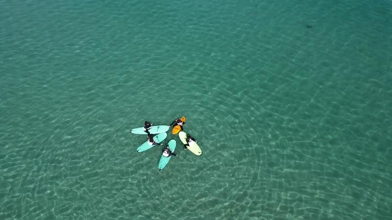 Grupo de jóvenes en el agua con sus tablas durante una sesión práctica en el campamento surf cantabria