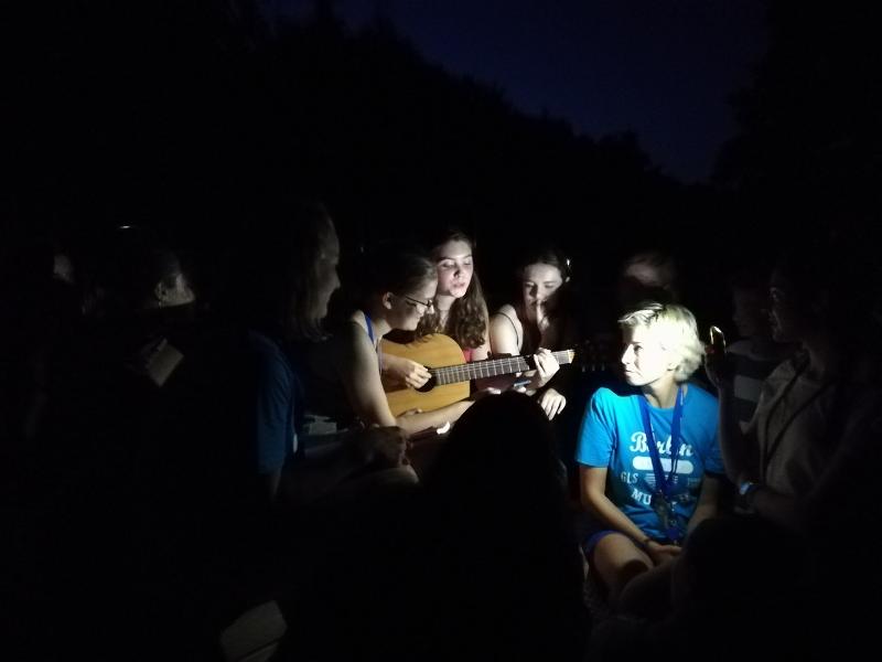 Jóvenes cantanto alrededor de una chica tocando la guitarra en una velada nocturna en campamento alemania verano