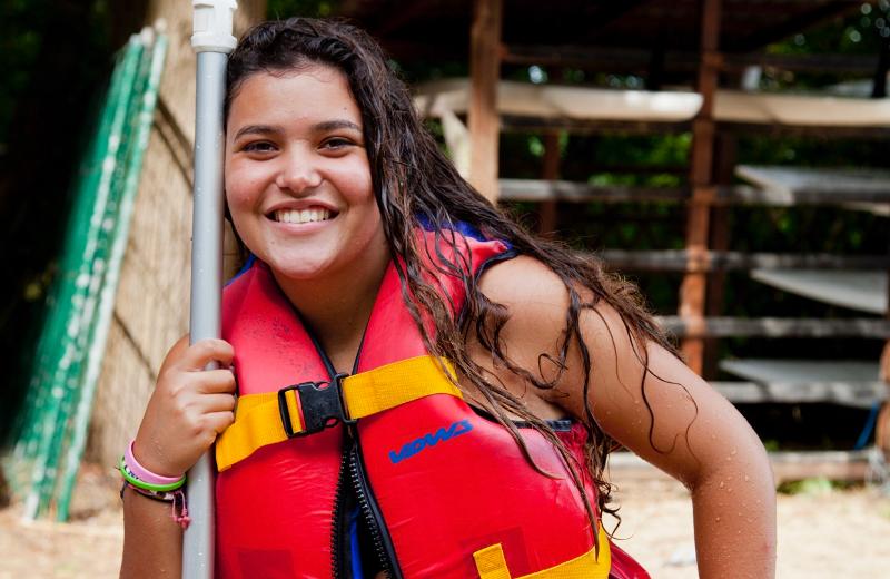 joven con chaleco salvavidas agarrando un remo con el pelo mojado y sonriendo en la orilla de un campamento alemania verano