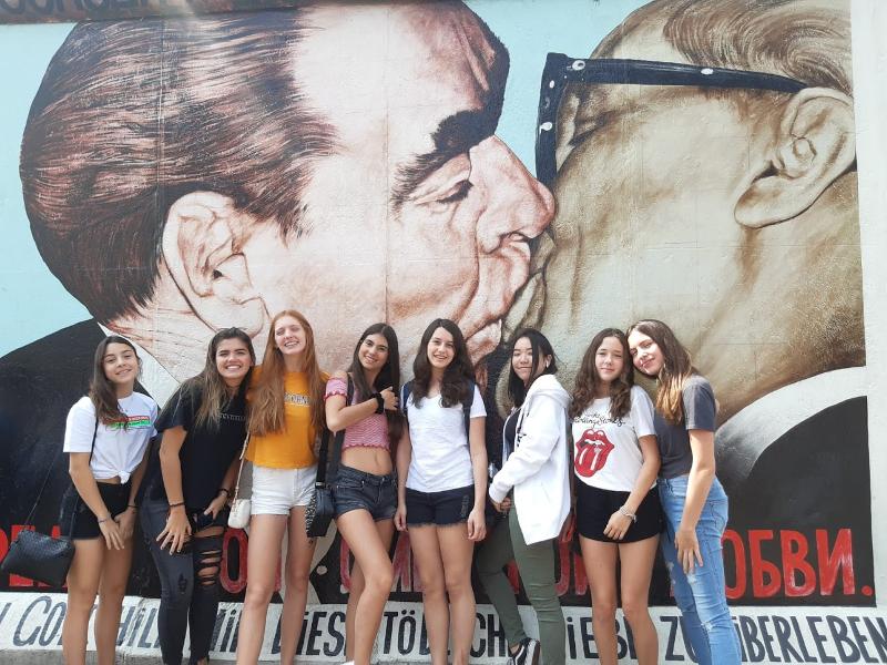 Grupo de campers posando con amigas frente al east side gallery en el muro de berlin en campamento aleman