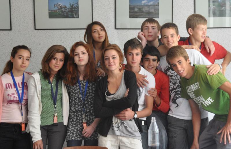 Grupo de jóvenes posando juntos en una clase con fotografias en la pared en un campamento en aleman