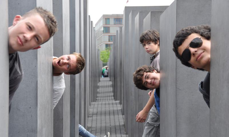 Chicos jóvenes posando en monumento de berlin sacando la cabeza entre los cubos de hormigón en campamento aleman