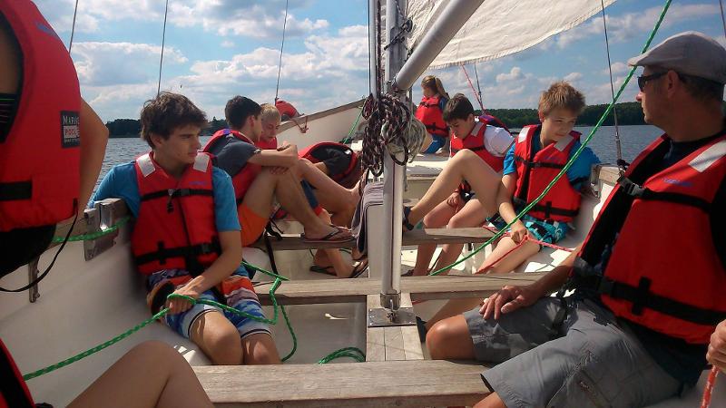 Jóvenes sentados dentro de un barco velero con monitor de navegación y salvavidas en el agua en campamento de verano alemania