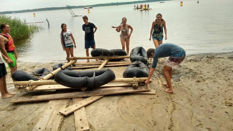 Jóvenes construyendo embarcación de madera con flotadores y arrastrándolo hacia el agua desde la orilla del campamento de verano alemania