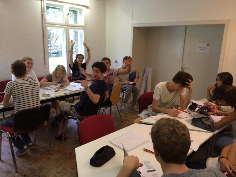 Grupo de alumnos entusiasmados en el aula con material de trabajo y libros en la mesa en curso de idiomas en alemania