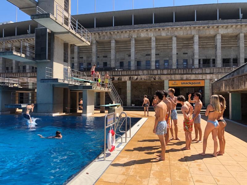 Jóvenes disfrutan de la piscina olímpica y miran a sus compañeros saltar desde el trampolín al agua en curso de verano en alemania