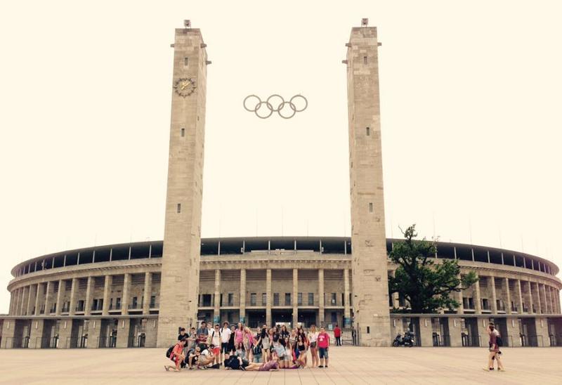Grupo de campistas posan en las afueras del estadio olímpico entre las dos torres principales y los anillos olímpicos en curso idiomas alemania